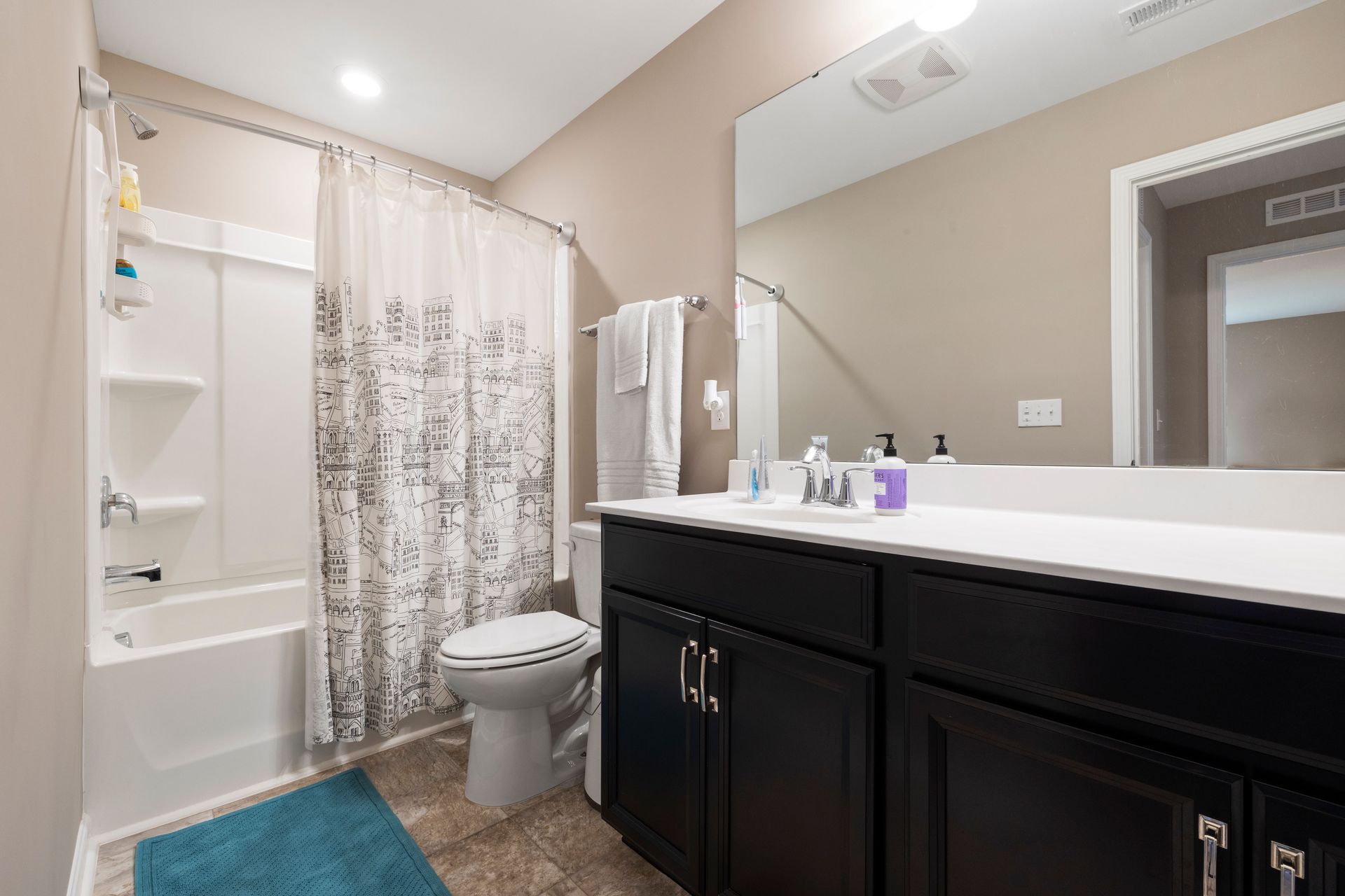 Clean and modern bathroom interior featuring a white bathtub, sink, and black cabinetry with a large mirror.